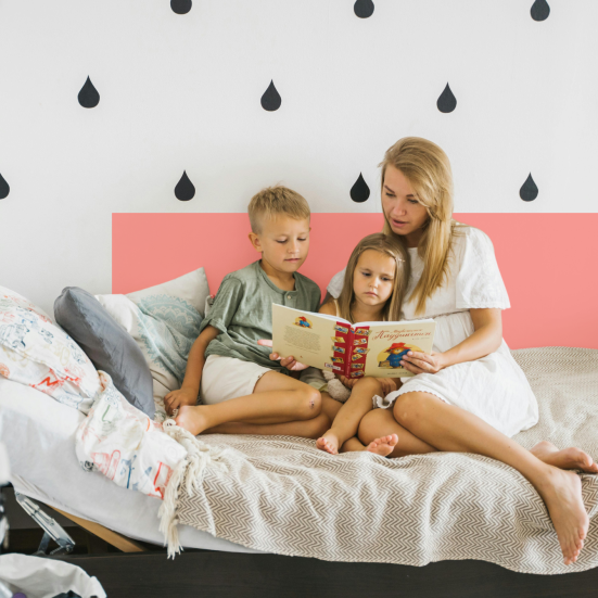 Mor i seng læser med to børn