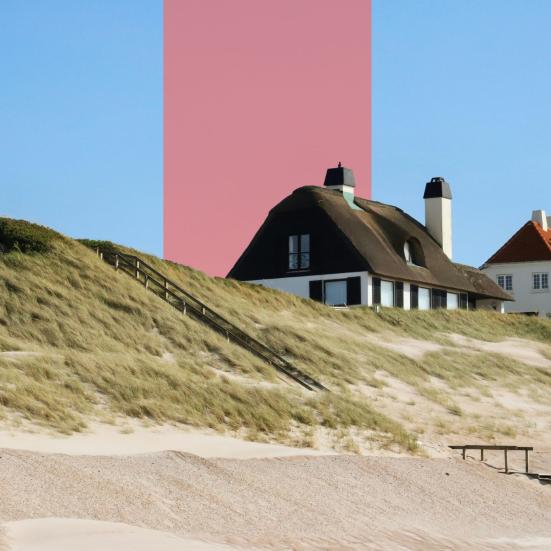 Sommerhuse ligger bag klitter ved en sandstrand under blå himmel.