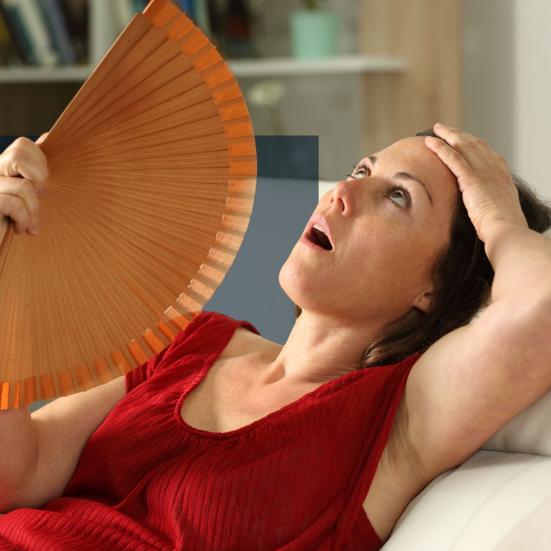 Kvinde, der sidder i en sofa og vifter sig med en håndvifte.