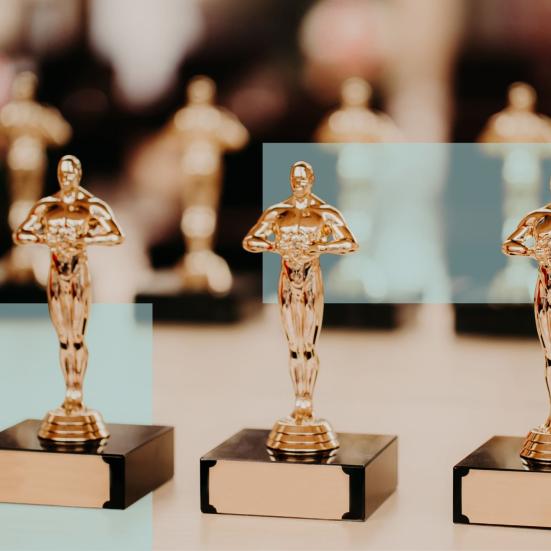Tre prisstatuetter i forgrunden med flere lignende statuetter bagved.
