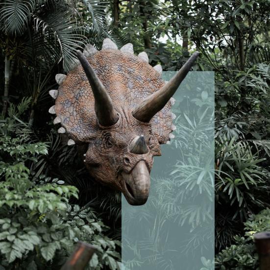 En hornet dinosaur stikker hovedet frem mellem tæt, grøn jungle.