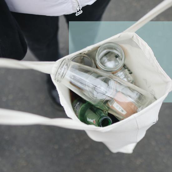 En person bærer en stofpose med tomme glasflasker og glas set oppefra.