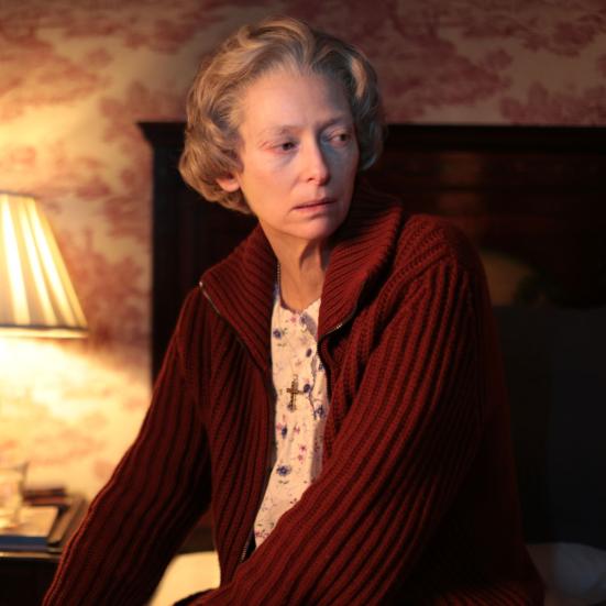 Stillbillede af Tilda Swinton fra filmen, siddende på sengekant i dæmpet belysning