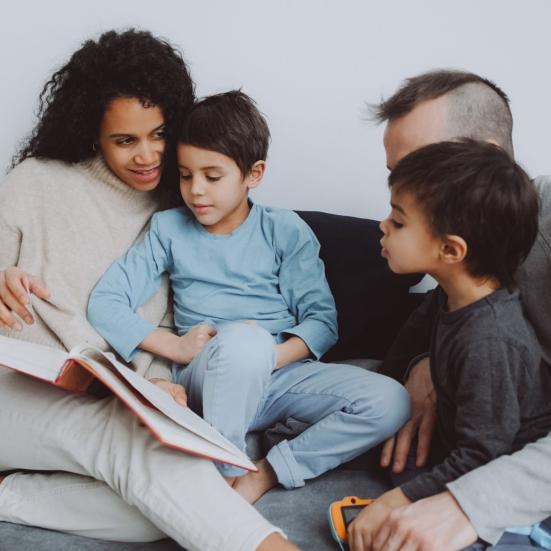 Familie sidder sammen i sofaen og læser en bog højt.