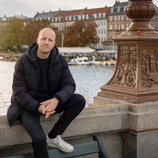 Mathias Stougaard sidder ved Dronning Louises Bro med sø og by i baggrunden.