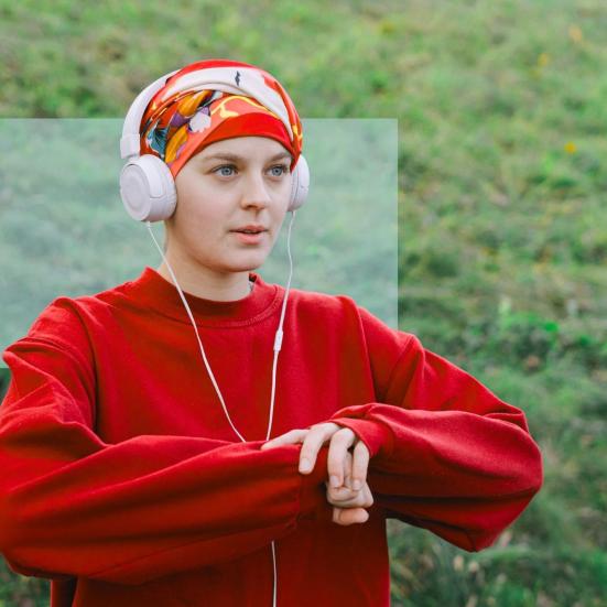 Person i rød sweatshirt og hovedtørklæde lytter til høretelefoner udendørs.