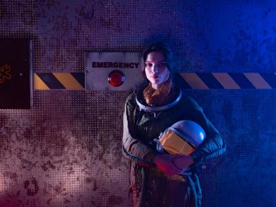 En kvinde iført rumdragt står foran en rød emergency knap