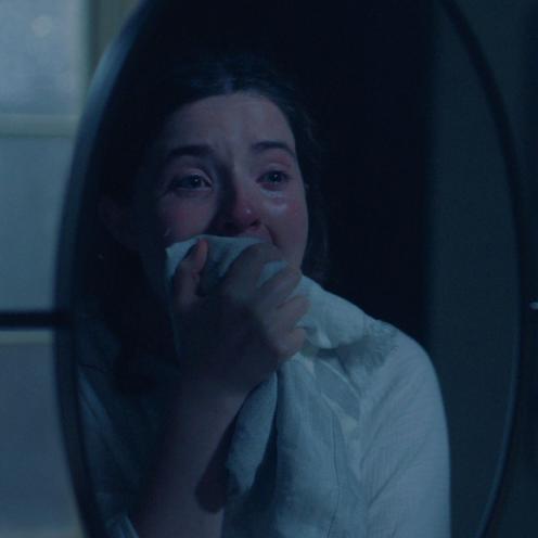 Nærbillede af en grædende kvinde, der dækker munden med et stykke stof.