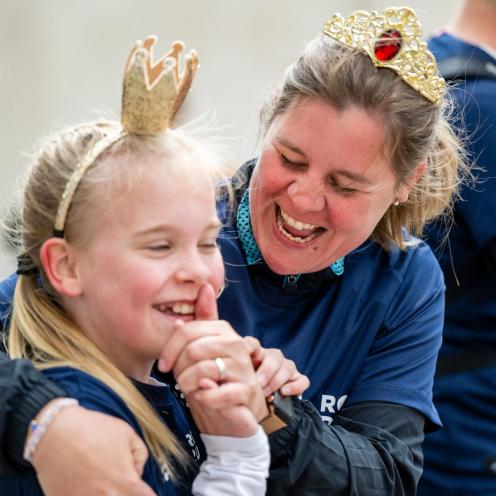 Kvinde og barn i Royal Run-trøjer griner sammen og har små kroner på.