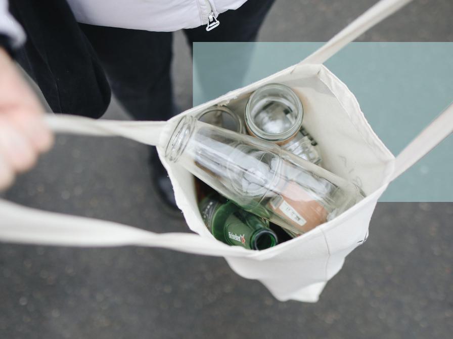 En person bærer en stofpose med tomme glasflasker og glas set oppefra.