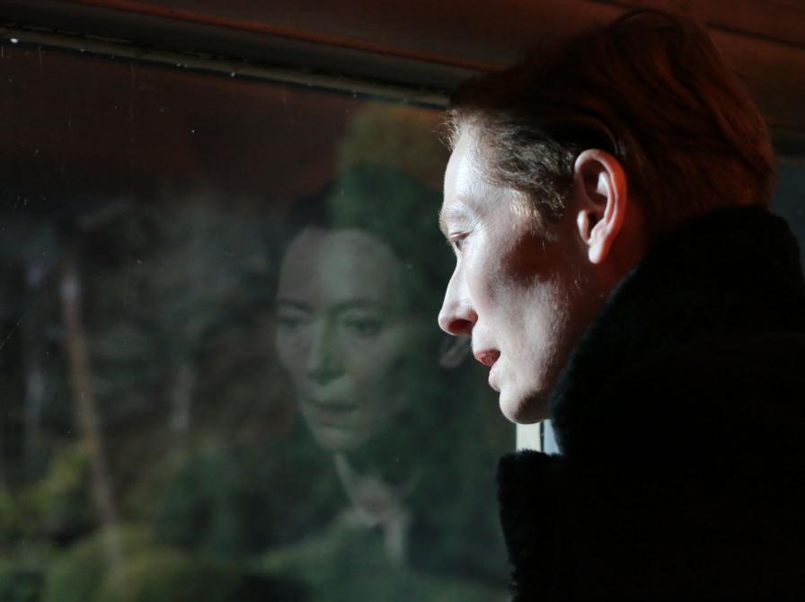 Mørkt stillbillede fra filmen af Tilda Swintin, set i profil, reflekteres i rude