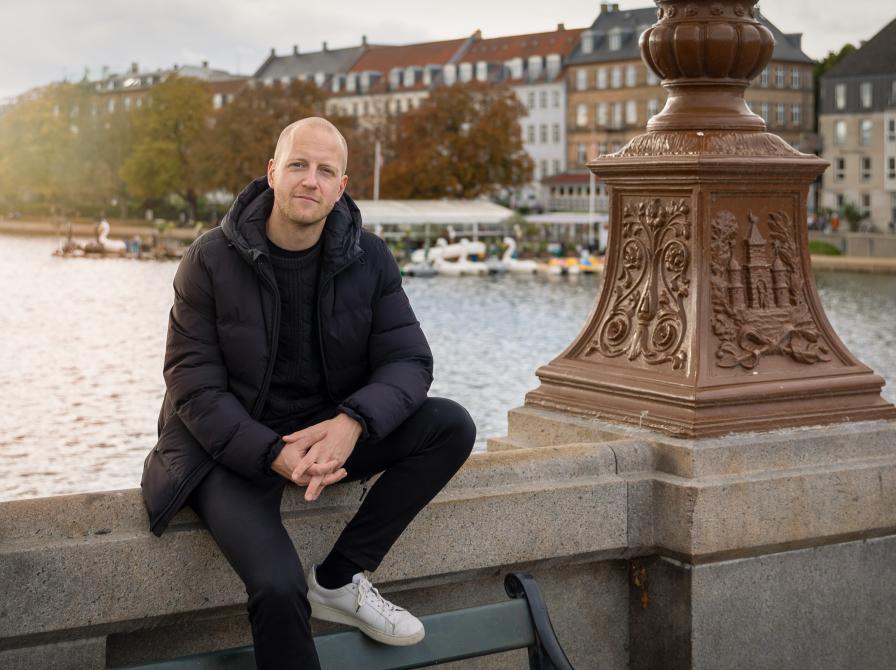 Mathias Stougaard sidder ved Dronning Louises Bro med sø og by i baggrunden.