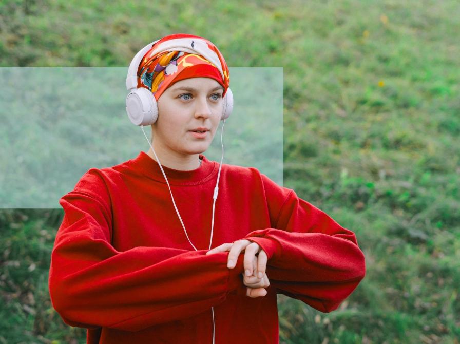 Person i rød sweatshirt og hovedtørklæde lytter til høretelefoner udendørs.