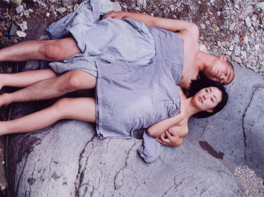 Mand og kvinde ligger på stranden ved siden af hinanden under et tæppe.