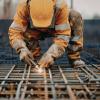 Arbejder i orange arbejdstøj og hjelm svejser metal, mens gnister flyver.