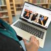 Foto af Ditte, som holder en tændt og opslået bærbar computer i hænderne, men man kan kun se Dittes hånd og lidt af hendes tøj. På computerens skærm ser man, at hun er inde på Service95 Book Clubs hjemmeside, hvor der blandt andet er billeder af Dua Lipa som poserer med forskellige bøger. Der er fuld fokus på computeren og hjemmesiden. Baggrunden og er let sløret og viser fyldte bogreoler.