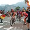 Cykelrytteren Fränk Schleck cykler på Alpe d'Huez under Tour de France 2006. Til højre ses jublende tilskuere. Én af dem med et tændt romerlys i hånden. Bag Schleck ses yderligere cykelryttere - Damiano Cunego og Eddy Mazzoleni.