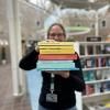 Tine står blandt fyldte bogreoler på Hovedbiblioteket. Hun holder syv af de omtalte bøger i denne artikel frem for sig i en stak med bogryggene frem. Der er fokus på bogryggene, mens både Tine og resten af baggrunden, som viser biblioteksrummet, fremstår let sløret. Man kan ane, at Tine smiler.